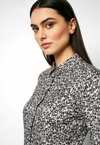 Bedruckte Bluse in Schwarz, Weiß und Grautönen; mit umschlagbarem Kragen und Knopfverschluss; glatte Textur mit einem strukturierten Schnitt.