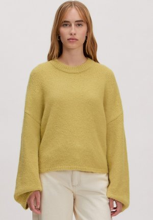 Geel gebreid trui met een ronde halslijn, brede mouwen en een gestructureerde afwerking, gecombineerd met lichtgekleurde broek.