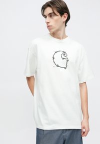 Λευκό βαμβακερό t-shirt με στρογγυλή λαιμόκοψη και κοντά μανίκια. Διαθέτει μαύρο γραφικό σχέδιο με αγκαθωτό σύρμα στο μπροστινό μέρος. Ξεκούραστη εφαρμογή.