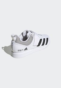 Zapatilla deportiva blanca con parte superior de malla, acentos grises y rayas negras. Correa ajustable y talón texturizado. Suela de goma para agarre.