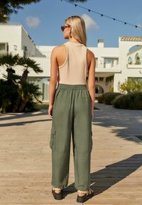 Helles beige ärmelloses Oberteil kombiniert mit olivgrünen Cargo-Hosen mit seitlichen Taschen, lockerer Passform und verstellbarem Bund. Schwarze Sandalen sind sichtbar.