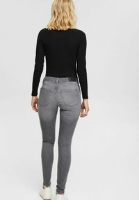 Gray slim-fit jeans with a high waist, back pockets, and a black waistband, paired with a fitted black long-sleeve top. Casual white sneakers.