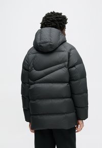 Czarna kurtka puchowa z kapturem, z poziomymi przeszyciami i elastycznymi mankietami. Gładki, błyszczący materiał o luźnym kroju.