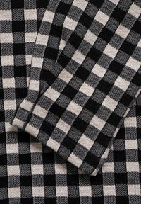 Black and beige woven fabric featuring a checked pattern with alternating squares. Soft texture, emphasizing a cozy appearance.