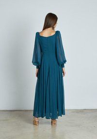 Türkisenes Kleid mit langen Ärmeln, quadratischem Rückenausschnitt, durchsichtigen Puffärmeln, Reißverschluss und fließender A-Linien Silhouette. Glatte Stofftextur.