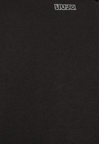 Pull en maille noire présentant un petit logo scintillant en strass au niveau de l'encolure. Texture douce avec une coupe ajustée.