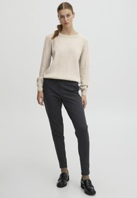 Maglione beige con texture, colletto rotondo e maniche lunghe abbinato a pantaloni a sigaretta grigio scuro e mocassini neri lucidi.