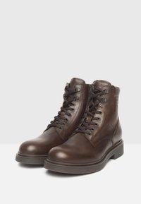 Un par de botas de cuero marrón con cordones hasta el tobillo y suelas gruesas sobre fondo blanco, anguladas para mostrar el frente y los lados exteriores.
