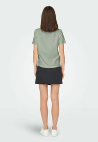 Lys grøn kortærmet t-shirt, i bomulds materiale, afslappet pasform, båret med en mørkeblå mini nederdel og hvide sneakers, set fra bagsiden.