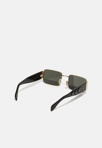Lunettes de soleil avec monture en métal doré, verres foncés carrés et branches en plastique noir. Les caractéristiques comprennent des détails texturés sur la monture et les branches.