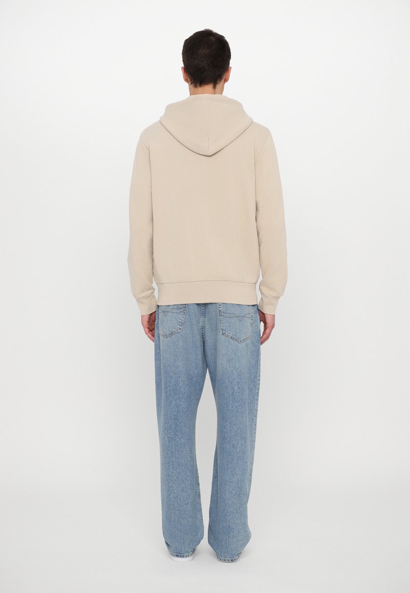 Lichtbeige hoodie met verstelbare trekkoord, ribgebreide manchetten en zoom. Gekleed met losse lichtblauwe denim jeans.
