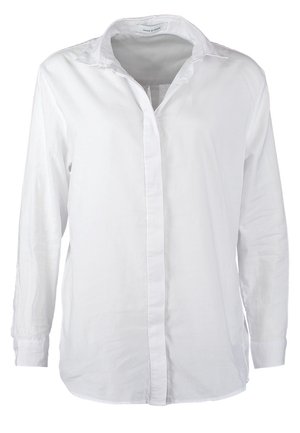 Personne portant une chemise blanche boutonnée, un jean skinny bleu clair retroussé, des talons hauts beiges et portant un sac bandoulière beige et marron.