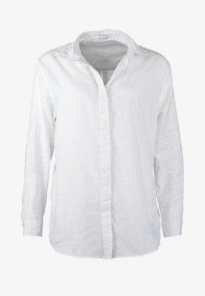 Personne portant une chemise blanche boutonnée, un jean skinny bleu clair retroussé, des talons hauts beiges et portant un sac bandoulière beige et marron.