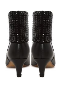 Botas de tobillo negras con tacón, de cuerpo de piel lisa y parte superior texturada con tachuelas. Presentan una puntera afilada y un tacón de 5 centímetros.