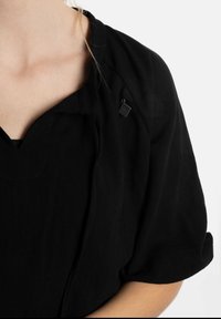 Zwart textiel top met een losse pasvorm, wijde mouwen en een ronde hals. Bevat een klein zwart label op de schouder, gladde textuur.