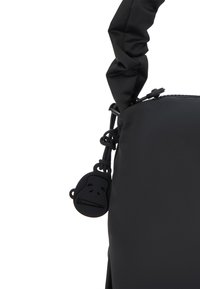 Sac en nylon noir avec une poignée froncée, doté d'une fermeture éclair et d'un pendentif en forme de visage de singe noir, arrondi, comme accent.