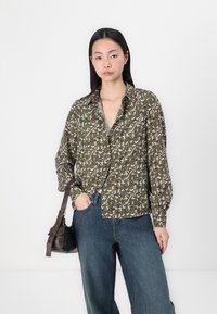 Grønnmønstret skjorte med lange ermer, prydet med blomstermønster, sammen med blå viddejeans og en brun skinnveske.