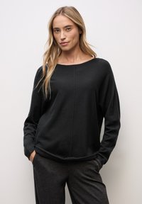 Top negro de manga larga con escote redondeado, tejido suave y costura destacada, combinado con pantalones gris oscuro.