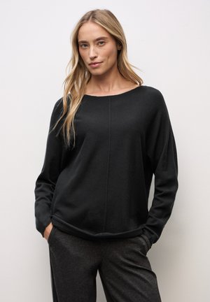 Maglia nera a maniche lunghe con scollatura arrotondata, tessuto morbido e dettagli di cucitura prominenti, abbinata a pantaloni grigi scuri.