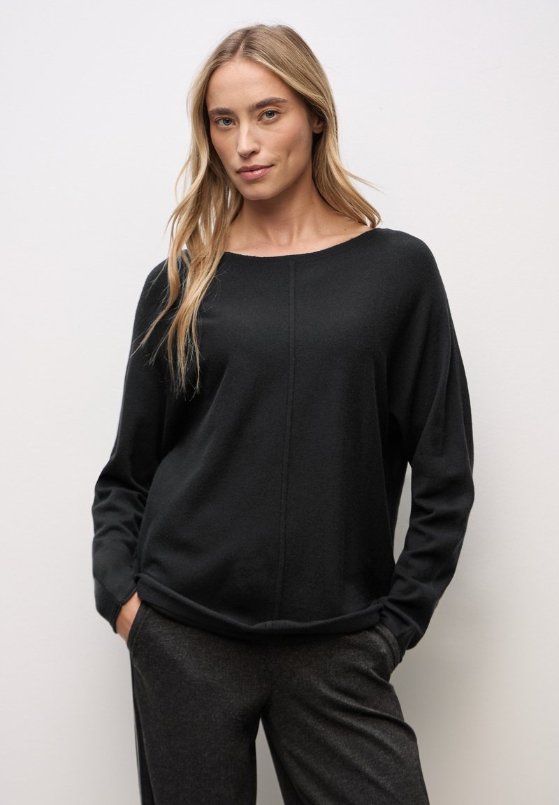 Top negro de manga larga con escote redondeado, tejido suave y costura destacada, combinado con pantalones gris oscuro.