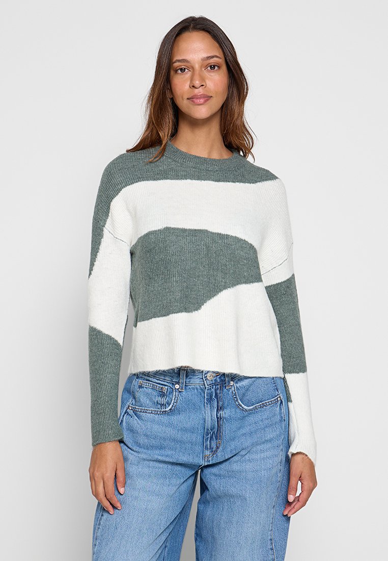 Häkel-Style Pullover in grün-weißen Streifen, mit rundem Halsausschnitt und langen Ärmeln, kombiniert mit blauen hochgeschnittenen Jeans.