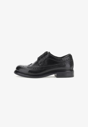 Chaussure de ville en cuir noir avec des détails brogue, bout rond et semelle plate. Dispose de six œillets pour les lacets et d'une finition lisse et polie.