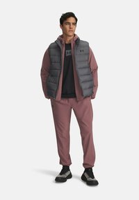 Men's athletic outfit featuring a gray puffer vest over a black shirt, paired with mauve jogging pants and black and gray sneakers.