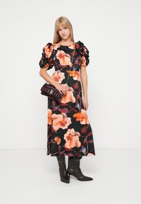 Μαύρο φορεμα με λουλούδια σε πορτοκαλί και μωβ απόχρωση, φουσκωτά μανίκια και μακριά σιλουέτα. Συνδυάζεται με μια μαρόνο χιαστί τσάντα και καφέ μπότες.