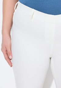 Pantalones blancos hechos de una tela ligera y texturada con una cinturilla elástica y un frente plano. Mano descansando sobre el muslo como referencia de tamaño.