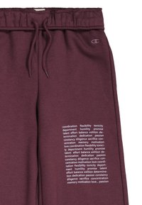 Pantalones de chándal color marrón oscuro con una cintura elástica, cordón y texto impreso en blanco que presenta varias palabras motivacionales en la pierna izquierda.