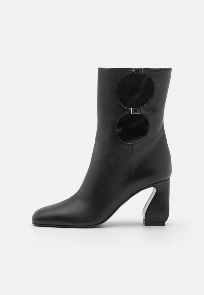 Black leather ankle boot with a pointed toe, unique round cutout detail at the back, and a chunky heel with a distinctive design.