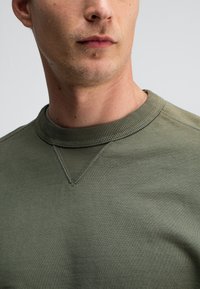 Olijfgroene sweatshirt met geribbelde ronde hals, textuurstof en zichtbare stiksels, met een klassiek ontwerp en een aansluitende pasvorm.