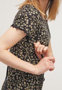 Czarna sukienka z kwiatowym wzorem w białe i żółte stokrotki. Krótkie rękawy z koronkowym wykończeniem, dopasowany krój w talii i zwiewna spódnica.