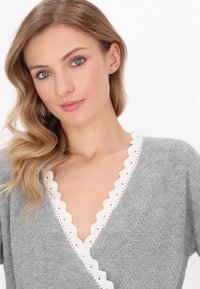 Cardigan grigio lavorato a maglia con un colletto di pizzo bianco a zig-zag e maniche lunghe. Texture morbida con una vestibilità rilassata.