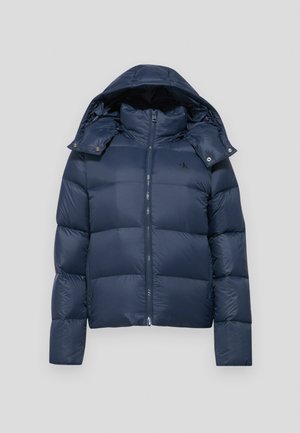 Tumedat sinine puhvjaktooni, millel on lukuga kinni panemine, eemaldatav kapuuts ja nuditud disain. Vasakul rinnal asub logo ja nupuga kaunistused.