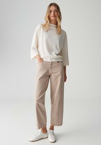 Roomwit ribgebreide trui met wijde mouwen, gecombineerd met lichtbeige wijde broek en witte sneakers, met een casual pasvorm en textuur.