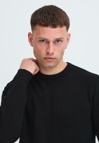 Zwart gebreid sweater met een geribbelde halslijn, voorzien van lange mouwen en een aansluitend ontwerp. Een zachte textuur en subtiele warmte zichtbaar in de stof.