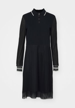 Musta mekko, jossa on poolopaita-kaarroke, pitkät läpinäkyvät hihat ja kerrostettu verkkohame. Mukana napitus ja raidalliset hihasivut.
