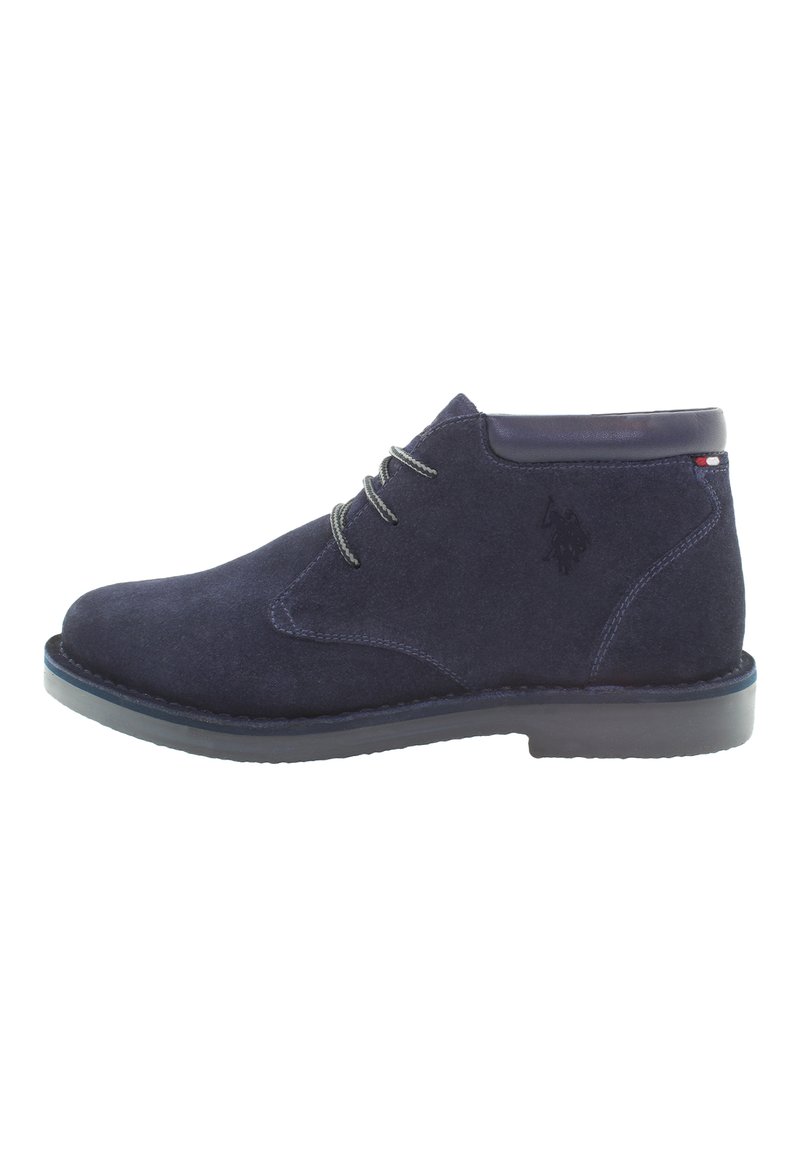 Las botas de ante azul marino hasta el tobillo cuentan con una punta redondeada, cordones frontales con cordones grises y una suela negra en contraste. Logo embossed en el lateral.