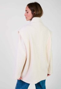 Crème-kleurige oversized jas van zacht materiaal, met een hoge kraag en verlaagde schouders, een gladde textuur en minimale naden.
