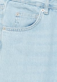 Tissu en denim bleu clair en gros plan montrant la poche avant avec rivets et passants pour ceinture sur un jean.