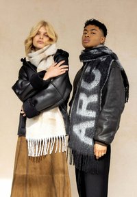 Veste en cuir noir avec des poignets en fourrure, foulards de couleur claire et à motifs, et une jupe en suède marron avec des coutures pour le détail.