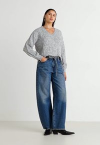 Pull en tricot gris avec un col en V et un motif en losange, associé à un jean large taille haute bleu et des bottines noires pointues.