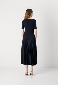Navy pleated dress with a ribbed bodice and short sleeves. Smooth texture and a flared skirt, paired with black strappy heels.