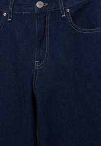 Mørkeblå denimjeans med knaplukning og kobberfarvet syning. Modellen har fem-lags-lomme-design og glat, tekstureret stof.