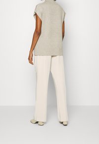 Pull en beige à manches courtes avec un col haut, associé à un pantalon large crème et des chaussures à talons blocs de couleur claire.