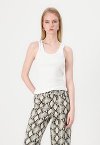Top de tirantes blanco con escote redondo, combinado con pantalones de pierna ancha en patrones de serpiente en tonos beige y negro. Diseño sencillo, corte casual.