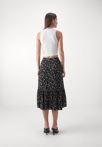 Top de tirantes blanco ajustado y una falda midi negra con estampado floral y dobladillo con volantes. La falda presenta pequeños patrones de flores coloridas.