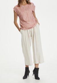 Červený vzorovaný top s krátkým rukávem a volným střihem, kombinovaný s lehkými béžovými kalhotami s širokými nohavicemi. Černé kotníkové boty outfit dokončují.