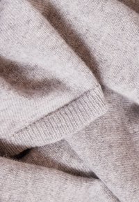 Tissu tricoté gris clair avec une texture douce, comprenant un poignet côtelé et de légères variations de teinte sur l'ensemble.